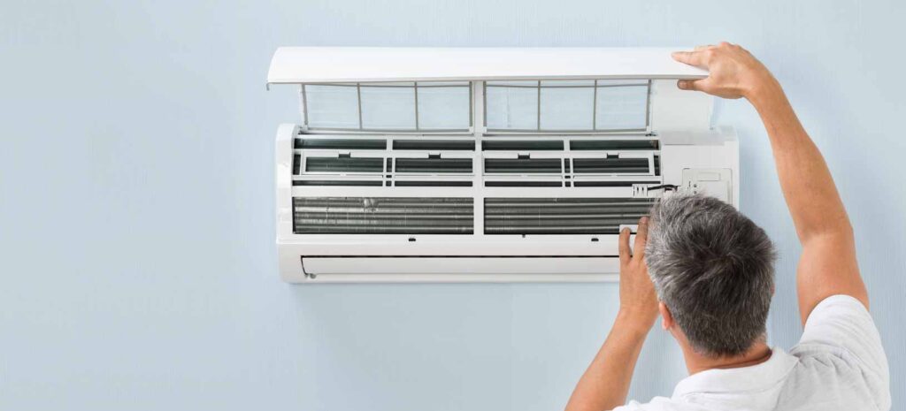 Man looking into air conditioning unit | Featured image for the air conditioning electrician page.